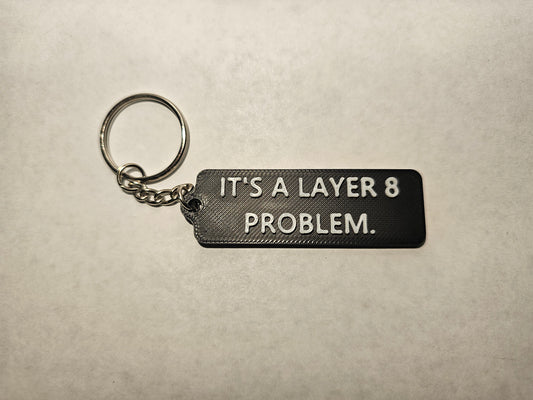 Close-up of a humorous 'It's a Layer 8 Problem' keychain designed for IT professionals and tech experts. The keychain features a playful reminder that tech issues often stem from user error (Layer 8) rather than hardware or network issues (Layers 1-7). Perfect for IT support, network administrators, and anyone in tech who has encountered the dreaded 'user problem.